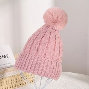 Detail of pink knit beanie featuring cable knit texture and large fluffy pom-pom detail