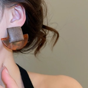 Close-up of geometric resin and wood earrings worn by a model in warm lighting