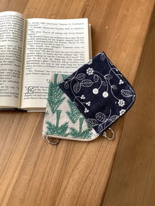 Close-up of linen embroidery coin purses with floral patterns and metal D-rings on wood