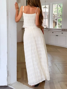 Detail of white pleated camisole and maxi skirt set featuring textured fabric on model