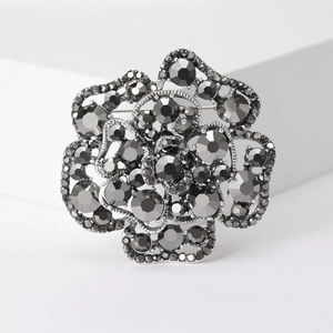 Close-up of a silver floral brooch with dark gray pavé crystals on a white pedestal