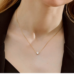 Close-up of a brilliant round zircon pendant on a gold chain worn on a model's neck