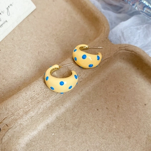 Detailed view of yellow C-shaped hoop earrings with blue polka dot resin finish