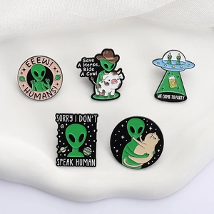 Five unique alien and UFO enamel pins set on a white textured background for clothing