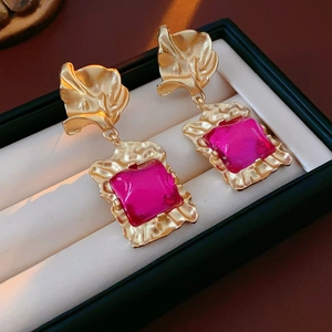 Macro detail of vintage gold earrings with rose red square gemstones on a dark background
