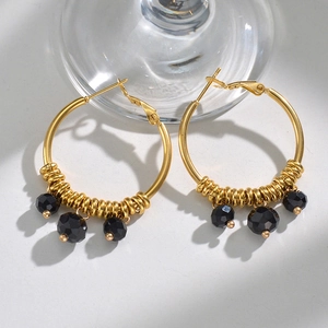 Macro shot of gold U-shaped hoop earrings with faceted black beads and small gold rings