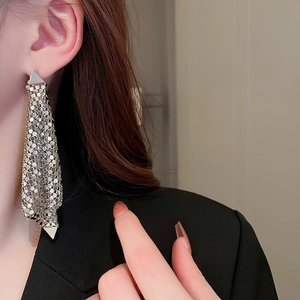 Détail de boucles d'oreilles triangulaires en métal argenté avec pompon en maille