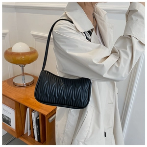 Detail of stylish black quilted shoulder bag with unique pleated texture on a model