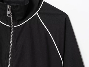 Detail of black nylon puffer jacket showing silver metal zipper and white piping accents