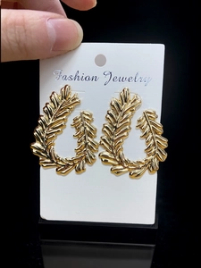 Macro shot of large golden leaf-shaped earrings with metallic texture on display card