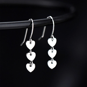 Macro shot of silver metal drop earrings with three heart-shaped sequins on black background