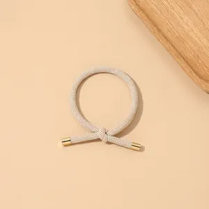 Close-up of beige ribbed hair tie with decorative knot and golden metal cylinder caps