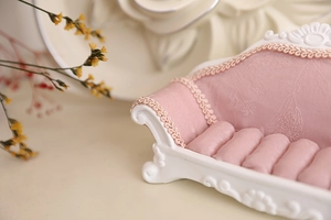 Detaillierte Nahaufnahme eines rosa Mini-Sofa-Ringhalters mit geprägtem Stoff und Spitze