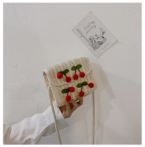 Detail of a beige woven straw bag with handmade 3D cherry accents and braided strap