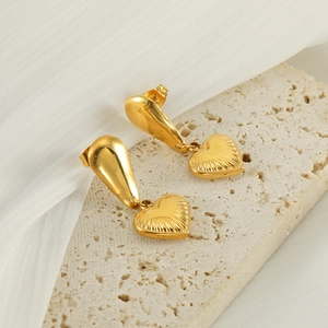 Vintage style gold heart drop earrings with radiant texture on stone and fabric background