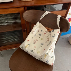 Close-up of beige cotton tote bag with colorful floral print hanging on a wooden chair