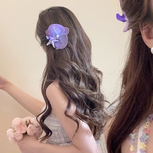 Detailed view of a purple fabric flower hair clip with pearl and starfish on a female model