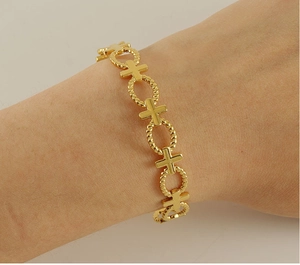 Close-up of a gold hollow cross and twist ring bangle on a woman's wrist