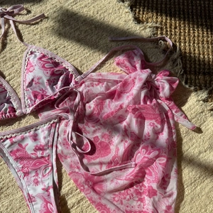 Détail à plat d'un bikini imprimé paisley rose avec paréo assorti et bords festonnés