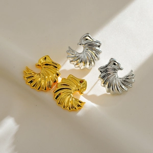 Elegant gold and silver fan-shaped metal stud earrings on white fabric texture