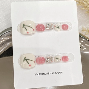 White and pink glitter press-on toenails with cherry patterns and rhinestones on a tray