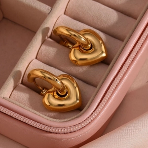 Macro shot of gold-plated heart pendant earrings resting in a pink silk jewelry box