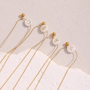 Detail of 18K gold plated necklaces with white shell-like beads showing G, L, R, X letters