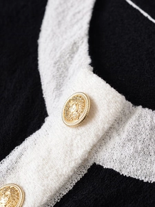 Detail of black knit fabric with white trim and embossed gold vintage crest buttons