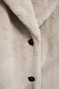 Detailed macro view of soft beige faux fur texture with two black buttons on long coat