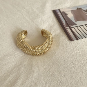Macro detail of gold lava-textured wide open cuff bracelet with irregular metal ridges