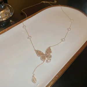 Gold plated butterfly necklace with freshwater pearls and tassels in a white dish