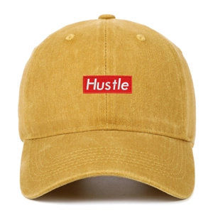 Close-up of yellow washed cotton baseball cap featuring red Hustle embroidery detail