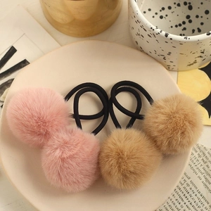 Detail of four fluffy faux fur pompom hair ties in pink and brown on a ceramic tray