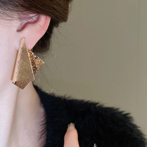 Close-up of irregular folded gold metal earrings worn on ear with textured finish