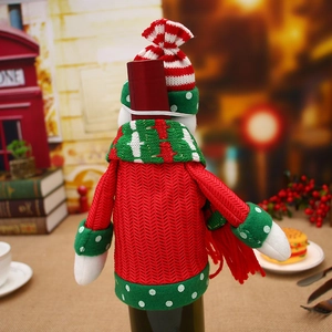 Detail of knitted Christmas wine bottle cover with red festive hat and scarf decor
