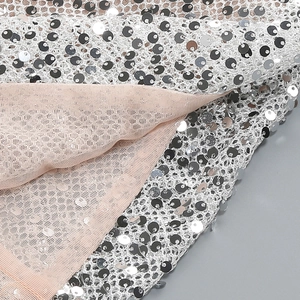 Macro detail of sparkling silver sequins on mesh fabric with a soft nude lining