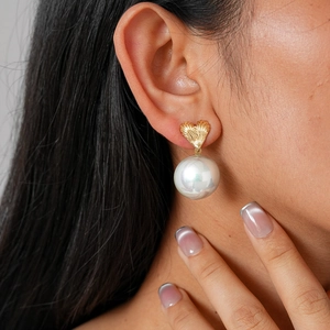 Elegant heart-shaped gold studs with large pearl drops, shown on a model's ear