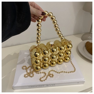 Χρυσό ακρυλικό τσαντάκι clutch με μεταλλικές σφαίρες και χάντρες πάνω σε βιβλίο