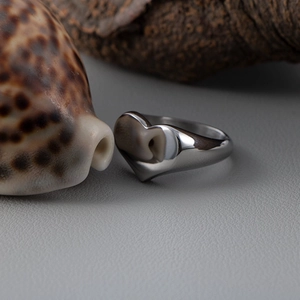 Polished silver heart ring displayed on gray leather with decorative seashell background