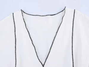 Gros plan du col en V avec surpiqûres noires contrastées sur un tissu textile blanc