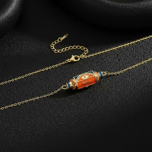 Macro detail of gold-plated necklace with orange enamel pendant and Evil Eye symbol