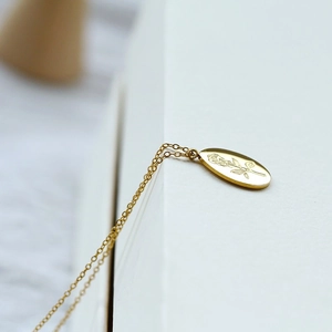 Detail of golden oval pendant with delicate rose engraving on a minimalist chain