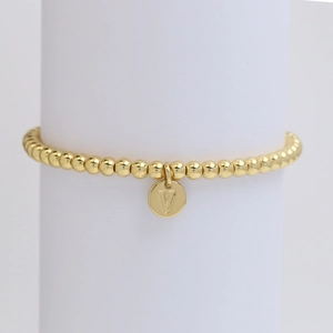 Close-up of golden beaded bracelet with a V letter pendant on a white display stand