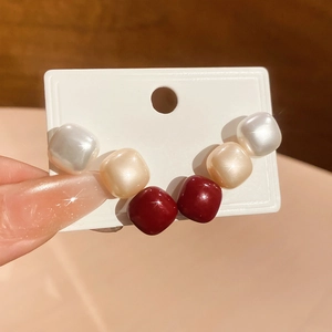 Close-up of geometric square stud earring set in pearl white, champagne gold, and burgundy