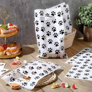 White plastic party gift bags with black paw prints and die-cut handles on a wooden table