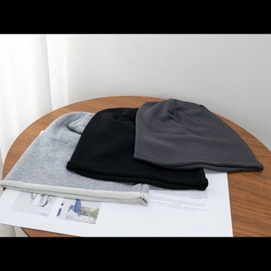 Three knit beanies in black, light grey and dark grey displayed on a wooden table