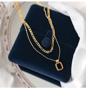 Close-up of double-layer gold necklace with black square pendant on velvet box