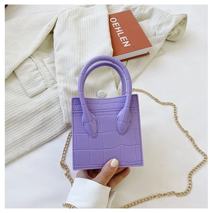 Detail of a purple croc-embossed mini square bag with dual handles and gold chain strap