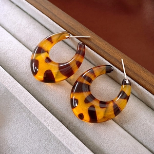 Detailed macro view of C-shaped tortoiseshell leopard print resin earrings on velvet