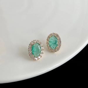 Gros plan de boucles d'oreilles fleur dorées avec gemme verte et halo de zircon
